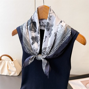Elegant black and white butterfly print silk scarf tied on a navy knit vest on a wooden hanger