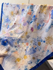Dettaglio di un foulard in seta con motivi floreali astratti e bordi blu scuro