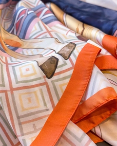 Détail macro du foulard en soie montrant l'ourlet orange et le motif équestre élégant