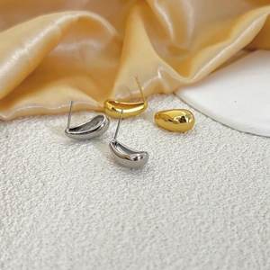 Detail of polished gold and silver water drop earrings on a white stone background