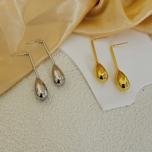 Gros plan de boucles d'oreilles gouttes polies en or et argent sur fond de soie