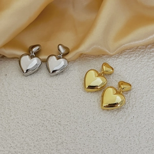 Boucles d'oreilles double cœur en or et argent polis sur fond de satin champagne
