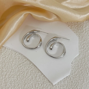 Macro detail of silver spiral drop earrings with metallic curves on white stone and silk