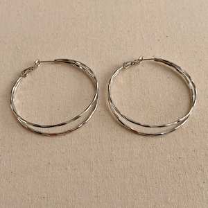 Close-up of silver double-hoop earrings with hammered texture on beige canvas background