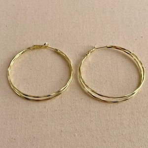 Detailed close-up of gold double-layered hoop earrings on a neutral beige canvas background