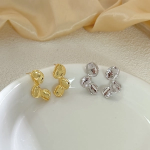 Irregular textured gold and silver drop earrings on a minimalist white ceramic tray