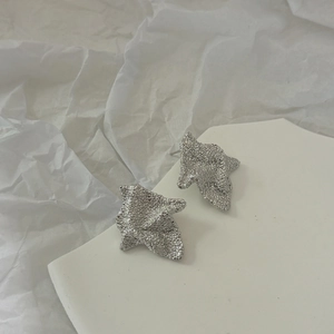 Close-up of matte silver irregular wrinkled earrings with a minimalist abstract design