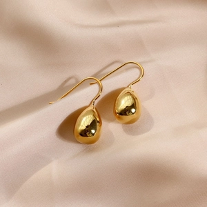 Polished gold water drop hook earrings resting on elegant beige silk fabric background
