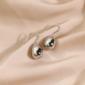 Polished silver teardrop hook earrings on silk background for minimalist style