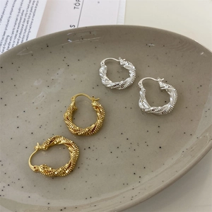Detailed close-up of gold and silver twisted rope hoop earrings on a ceramic plate