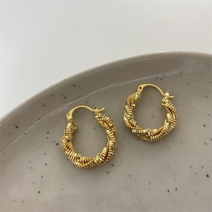 Close-up of double-layered gold twisted hoop earrings with textured beaded rope design