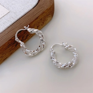 Detail of twisted silver earrings with textured spiral layers on minimalist cream backdrop