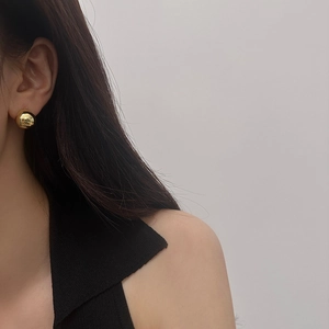 Close-up of minimalist golden spherical stud earrings with polished mirror finish on model