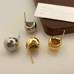 Detail of high-polish minimalist gold and silver bean stud earrings on a wood block