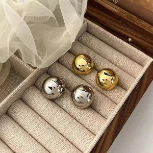 Polished gold and silver dome stud earrings displayed in a wooden jewelry tray