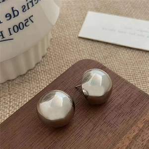 Macro shot of polished silver spherical stud earrings on dark wood with a mirror finish