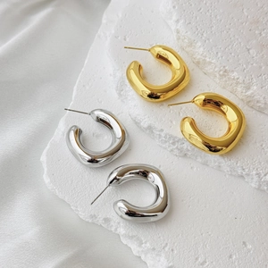 Polished gold and silver chunky hollow hoop earrings on a textured white stone surface