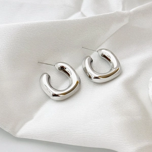 Polished silver geometric C-shape hoop earrings on white silk fabric for a luxury look