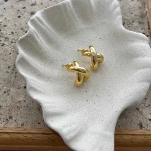 Detail of gold criss-cross earrings on a shell plate, high-polish fashion jewelry