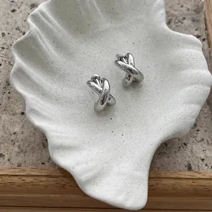 Chic silver crossover knot earrings displayed on a white shell tray with rock texture