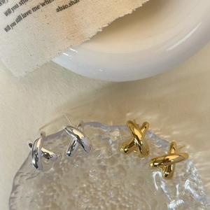 Detailed view of polished gold and silver X-shaped cross earrings on textured fabric