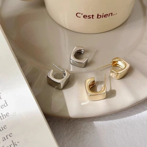 Detailed macro view of gold and silver square hoop earrings on a beige ceramic tray