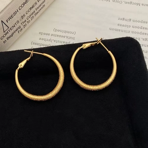 Detailed view of matte gold geometric hoop earrings with textured finish on velvet