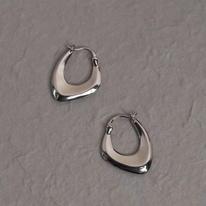 Minimalist irregular geometric silver hoop earrings on a dark grey stone surface