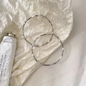 Détails des créoles torsadées argentées avec une texture unique sur un fond minimaliste chic