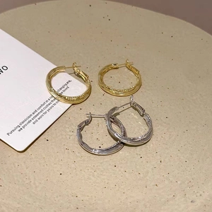 Detail of twisted double hoop earrings in gold and silver finish on a textured tray