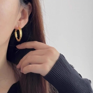 Macro shot of gold-plated double-layer braided hoop earrings worn on a model's ear