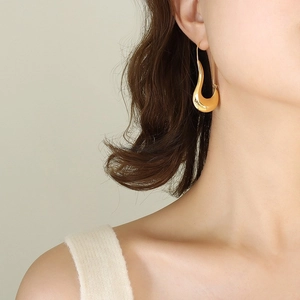 Boucles d'oreilles géométriques dorées incurvées et creuses portées par un mannequin