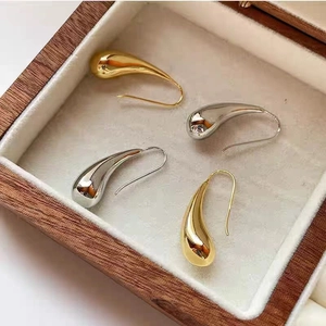 Polished gold and silver hollow teardrop earrings displayed on a beige velvet jewelry tray