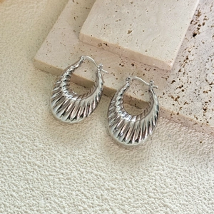 Gros plan de créoles en forme de corne plaqué argent avec texture striée sur pierre
