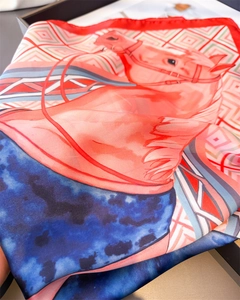 Gros plan d'un foulard en soie avec imprimé équestre, motifs géométriques et bord rouge