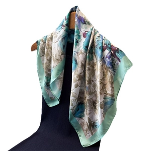 Carré de soie à imprimé floral vert pastel et bleu suspendu sur un cintre en bois naturel