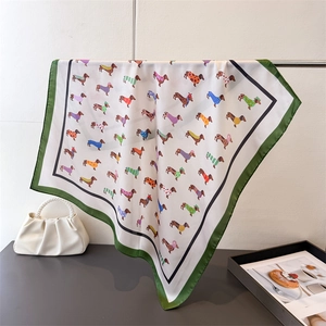 Détail d'un foulard en soie à imprimés teckel et ourlet vert suspendu à un support