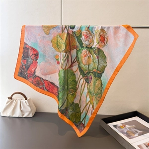 Artistic lotus print silk scarf with orange borders hanging on a metal rack