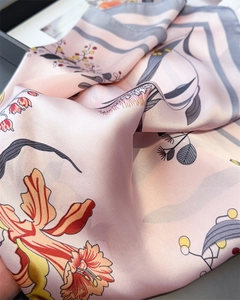 Detailed view of pink silk scarf showing smooth texture and orange floral print patterns