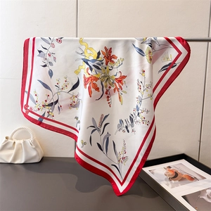 Detailed close-up of floral print silk scarf with elegant red border and draped texture