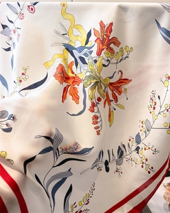 Detailed macro view of lightweight silk square scarf with floral lily prints and red borders