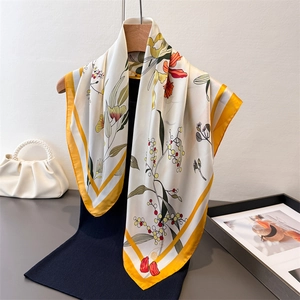 Floral print faux silk square scarf in cream with yellow borders hanging on wooden hanger