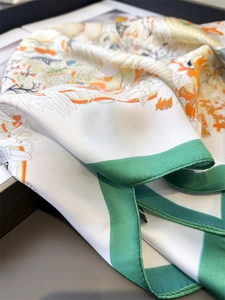 Close-up of silk scarf with orange floral prints and bright green borders on a dark desk