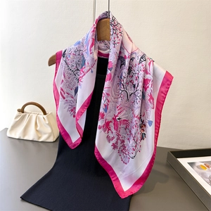 Floral print silk square scarf with pink borders draped over a black sweater