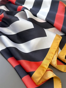Close-up of luxury satin silk scarf featuring vibrant red and black geometric stripes
