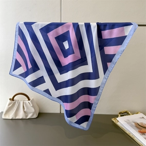 Detail of geometric stripe silk-like scarf draped elegantly by a stylish handbag