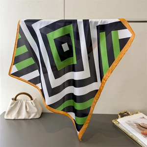 Detailed view of geometric square scarf with black green pattern and orange borders