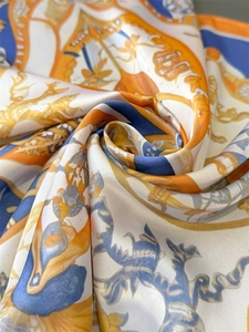 Dettaglio di un foulard in seta con motivi barocchi arancioni e blu effetto satin