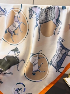 Detailed close-up of a silk scarf featuring classic equestrian horse prints and orange borders