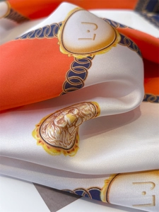 Detail of silk scarf showing orange and white patterns with golden lion crest and chains